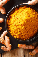 Ground fresh turmeric in a bowl and root close-up. Vertical top view