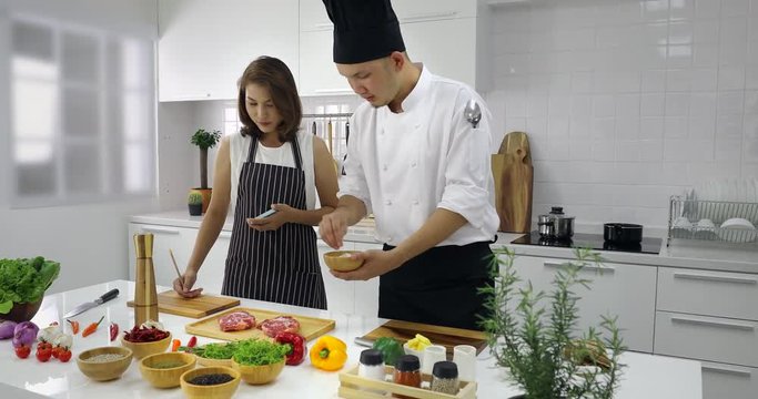 Asian chef teaching  Asian woman student how to marinate meat in cooking class, concept for cooking school.
