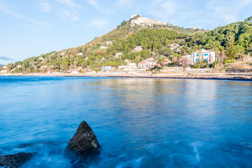 Fototapeta premium Long Exposure of the Mediterranean Sea Coast and a Medieval Hilltop Village with Blue Sky in Southern Italy