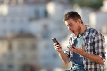 Amazed man checking smart phone content in a town