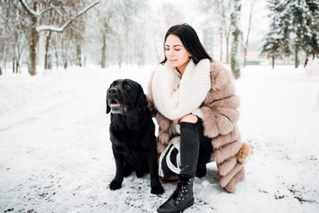 beautiful young girl with black hair in fur coat in winter outdoors, woman with big dog .snowy frosty day