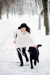 Fototapeta na wymiar beautiful young girl with black hair in white jacket in winter resting outdoors, woman playing with big dog snowy frosty day