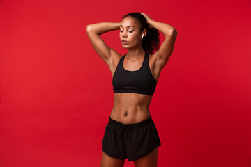Fototapeta na wymiar Beautiful young african sports fitness woman posing isolated over red wall background.