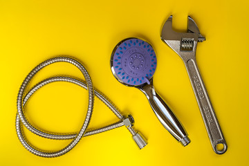 Metal adjustable wrench, new shower head and flexible hose on a yellow background. Handheld shower head with with function switch. Modern shower equipment. Plumbing works