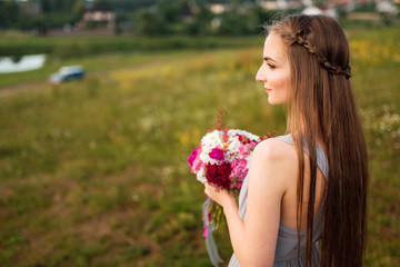Fototapeta premium Happy bride in beautiful white dress posing with bouquet of flowers on summer day. Wedding street photo session. Beautiful cheerful lifestyle portrait of bride
