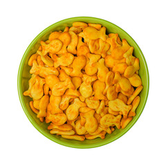 A lot of salty fish-shaped crackers in a green bowl, isolated on white background, close up, top view