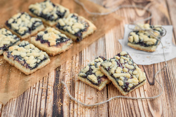 Shortbread cookies with blueberry jam on baking paper on wooden background. 