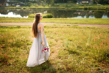 Fototapeta premium Happy bride in beautiful white dress posing with bouquet of flowers on summer day. Wedding street photo session. Beautiful cheerful lifestyle portrait of bride