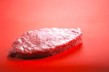 Raw beef steak on a red background. Close-up.