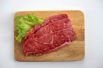 Beef steak on a wooden board. The steak is decorated with a leaf of green salad. Close-up. White background. View from above.