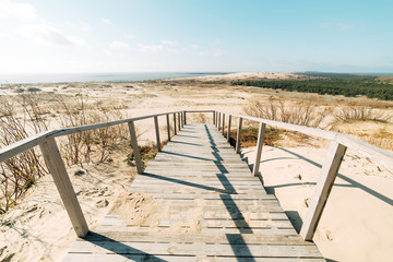 Fototapeta na wymiar Stairs to the beach. A wooden staircase leads to a wide sandy beach on the picturesque shore on a beautiful and windy summer day.