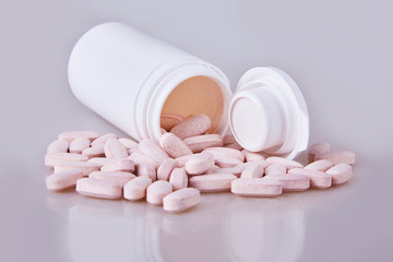 Vitamins (drugs) scattered and spilled out near an opened white plastic medicine bottle (container). Treatment with pills and medicine