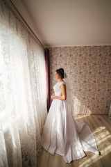 Charming bride stand in front of window. Girl stand by the window at her room