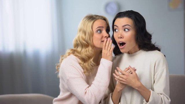 Woman whispering her exited friend about sale in shopping mall, discount