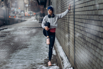 Athlete woman winter training outside in cold snow weather. Woman in headphones in snow day