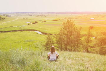 Young girl is doing yoga in the nature outdoors. Woman is practising asana on the hill in...