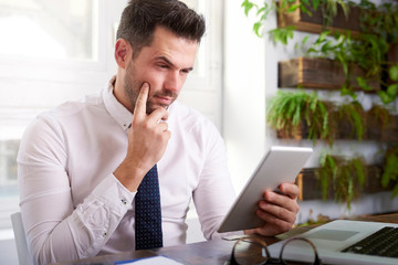 Naklejka premium Businessman using digital tablet and computer while sitting at desk and working in the office