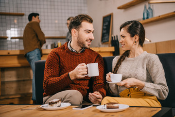 selective focus of couple holding cups and chatting in cafe