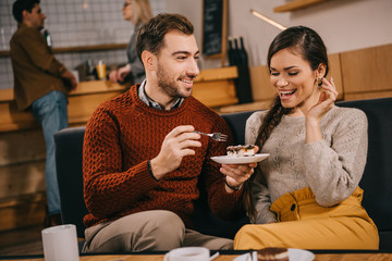 handsome man looking at surprised woman and holding cake in cafe