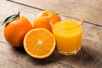 Fresh orange juice and oranges on wooden table