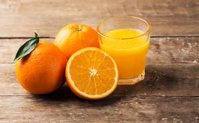 Fresh orange juice and oranges on wooden table
