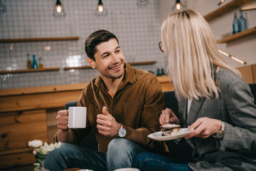 smiling man looking at girlfriend with cake in cafe
