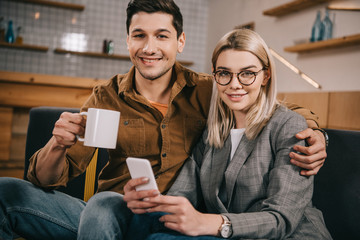 handsome man holding cup and hugging girlfriend in glasses