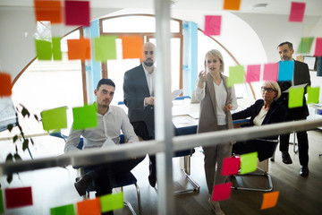 Group of analysts or brokers sitting in front of transparent board and discussing workflow on...