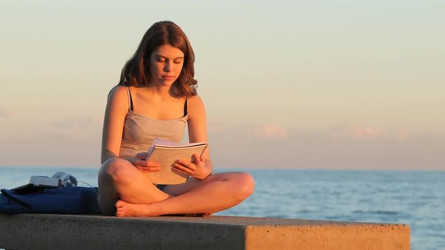 Full body portrait of a single student studying memorizing notes at sunset on the beach