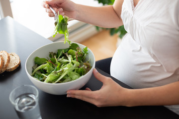 Pregnant woman eating a green salad at home