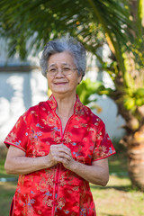 An elderly asian woman wearing Cheongsam red shirt standing and greeting in garden. Happy Chinese New Year.