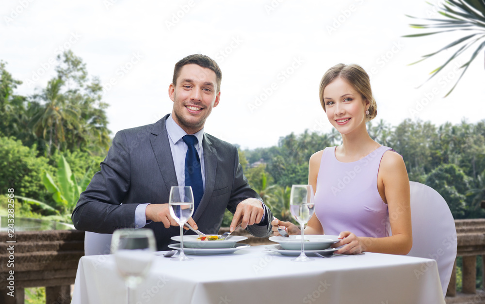 Wall mural people and leisure concept - smiling couple eating appetizers at restaurant over summer background