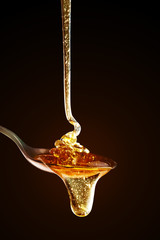Honey with gold color flows down from a spoon, on a dark background. Healthy eating. Diet. Selective focus.