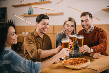 happy group of friends clinking beer near pizza in bar