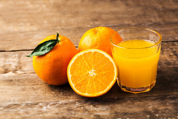 Glass of fresh orange juice with oranges on a vintage wooden background
