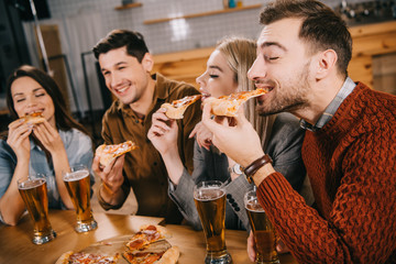 selective focus of happy friends eating pizza in bar
