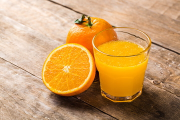 Glass of fresh orange juice with oranges on a vintage wooden background