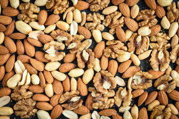 Nuts background of almonds, peanuts and walnuts with crumbs on black background.