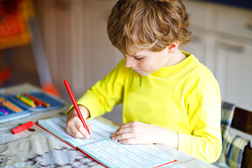 Happy smiling little kid boy at home making homework at the morning before the school starts....