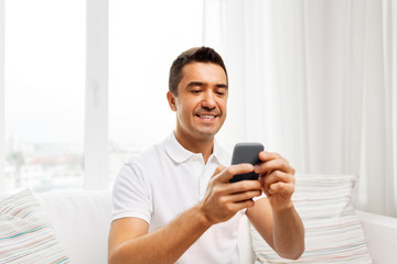 technology, people and communication concept - happy man with smartphone at home