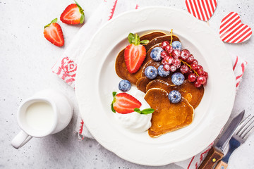 Pancakes in the shape of heart with berries, fruits and curd cream in a white plate, top view. Valentine's day concept.