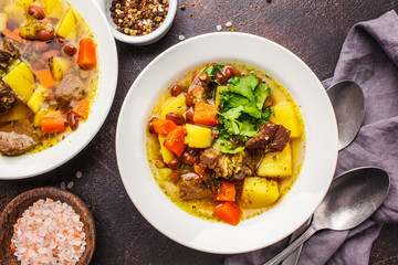 Traditional eintopf soup with meat, beans and vegetables in a white plate.