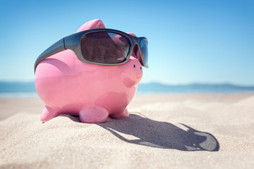 Piggy bank with sunglasses on the beach in Summer