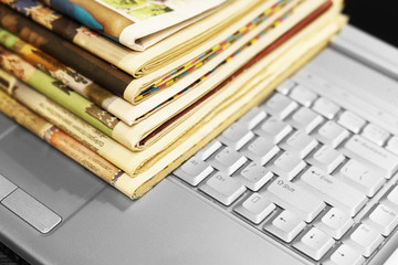 Newspapers and laptop. Pile of daily papers with news on the computer. Pages with headlines,...