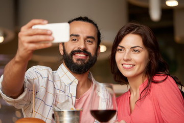 leisure, technology and people concept - happy couple having lunch and taking selfie by smartphone at restaurant