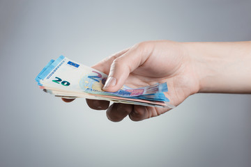 Hand holding stack of euros on gray background