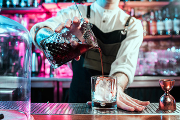 Expert barman is making cocktail at night club or bar. Glass of fiery cocktail on the bar counter against the background of bartenders hands with fire. Barman day concept