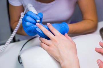 Closeup shot of a woman in a nail salon receiving a manicure by a beautician with electric nail file. Woman getting nail manicure. Beautician file nails to a customer