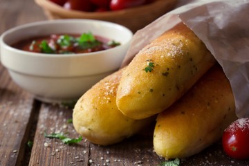 Close up of garlic bread sticks with marinara sauce on rustic wooden background