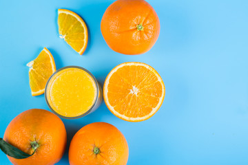 Orange juice in glass and slices of orange on blue background, top view